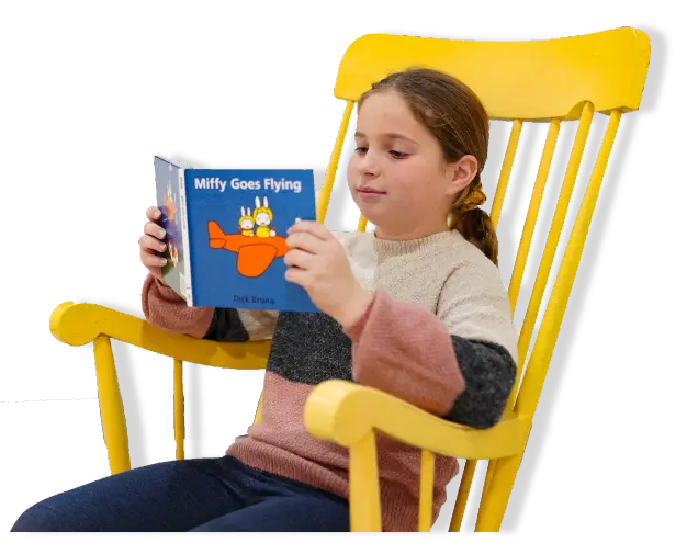 girl reading miffy goes flying, in a yellow rocking chair