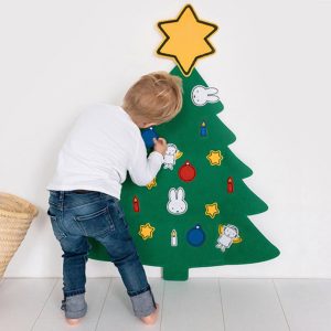 Small decorated Christmas tree with ornaments and a wooden Miffy decoration placed nearby on a light-colored floor.