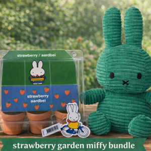 Large green knitted Miffy plush toy standing upright next to a green illustrated gift box and a smaller boxed item on a wooden surface.