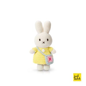 Knitted white Miffy rabbit in a pastel yellow dress, holding a small bag decorated with a flower.