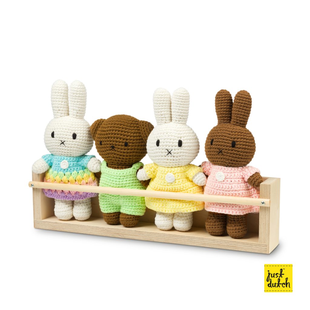 Wooden display stand holding four small dolls in a row with soft colored clothing.