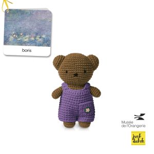 Knitted brown bear in a purple overall with a small flower.